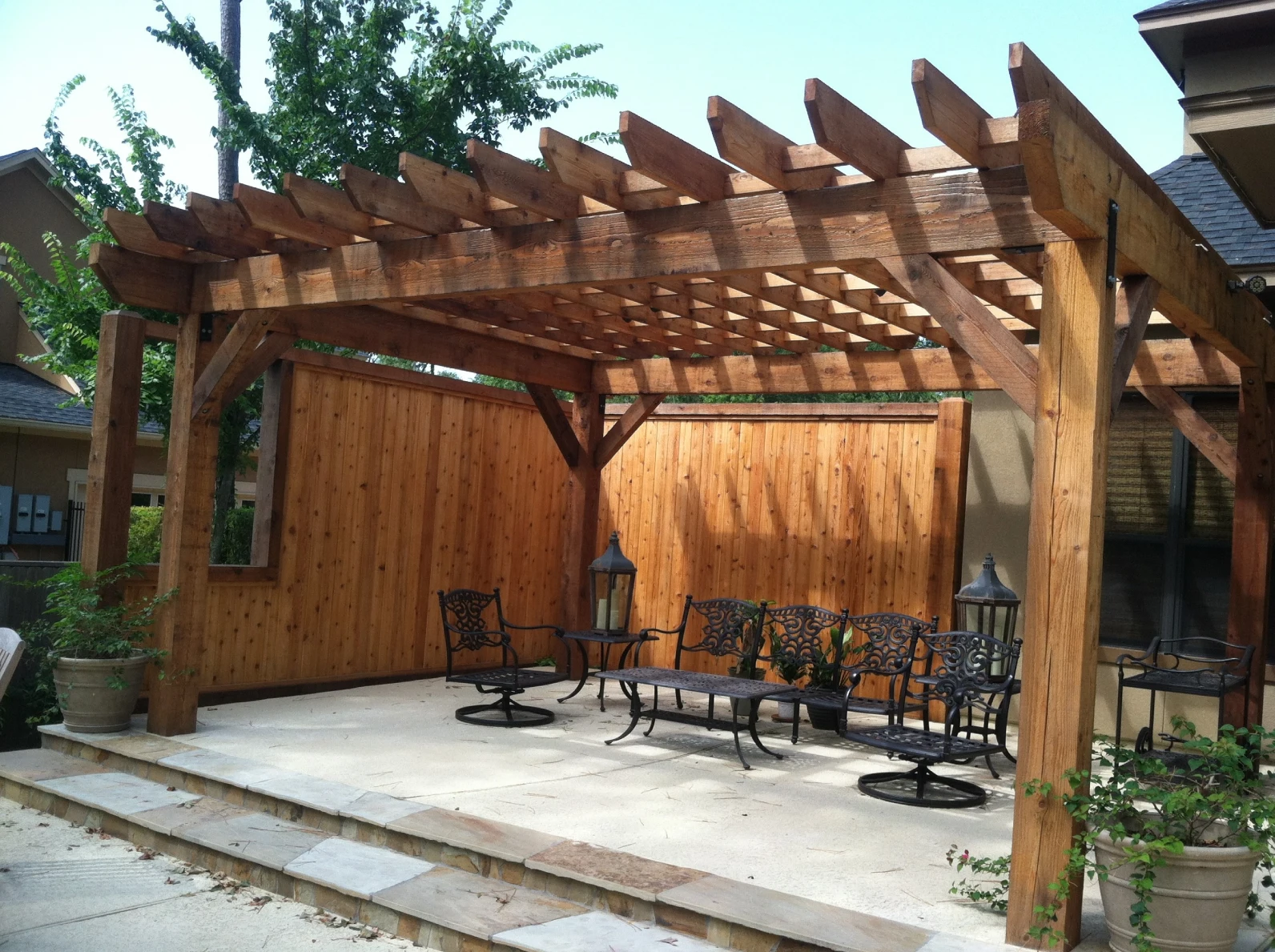 Outdoor patio with wooden pergola, wrought iron furniture, potted plants, and a wooden privacy screen.